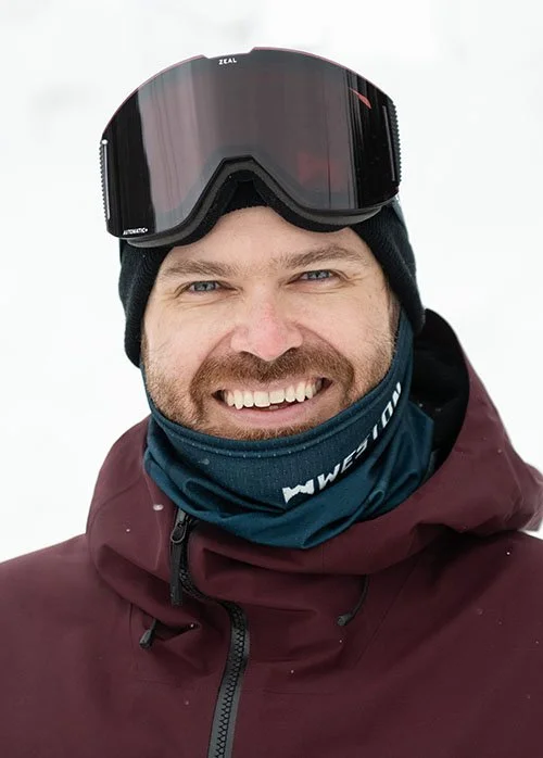 Sean Eno wearing a burgundy jacket and ski goggles in snowy conditions.